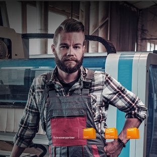 Tischlereien & Fensterbau Schreiner in Latzhose und kariertem Hemd vor einer CNC-Maschine in der Werkstatt. Schreinerpartner von Schreiner Bayern, Tischler Schreiner Baden-Württemberg und Tischler NRW