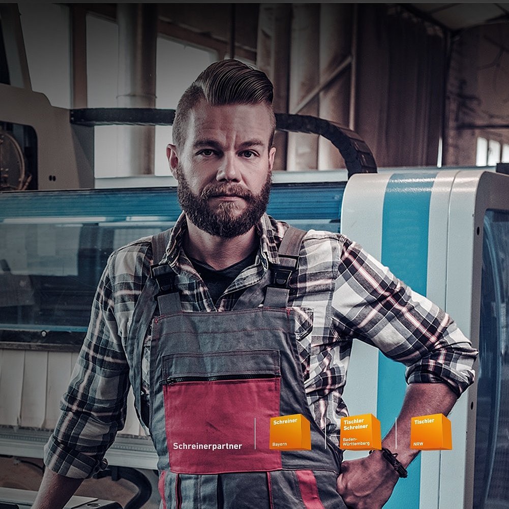 Tischlereien & Fensterbau Schreiner in Latzhose und kariertem Hemd vor einer CNC-Maschine in der Werkstatt. Schreinerpartner von Schreiner Bayern, Tischler Schreiner Baden-Württemberg und Tischler NRW